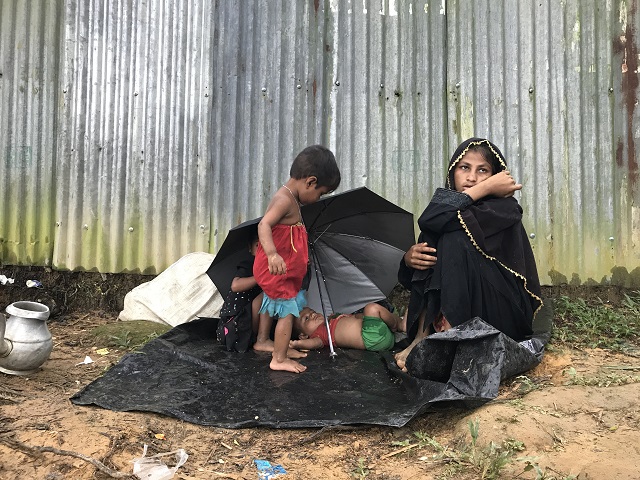路上にすわりこむロヒンギャの母親 雨に濡れたビニールシートに子どもが寝ている