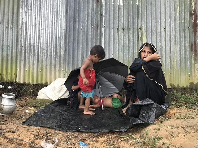 路上にすわりこむロヒンギャの母親　雨に濡れたビニールシートに子どもが寝ている